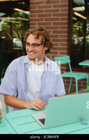 Young man smiling using laptop at outdoor cafe Stock Photo
