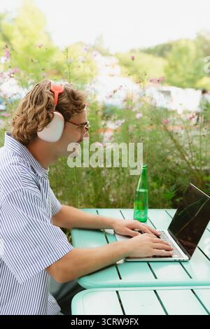 Man wearing headphones working laptop outdoors remotely Stock Photo