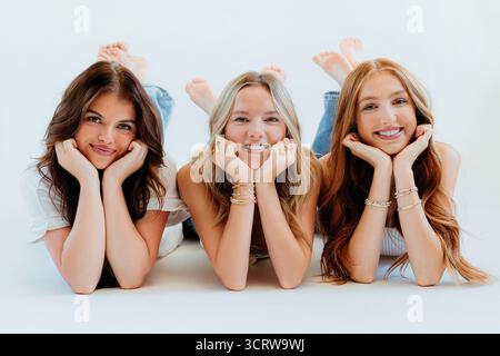 Three smiling women lie in denim and white on floor Stock Photo