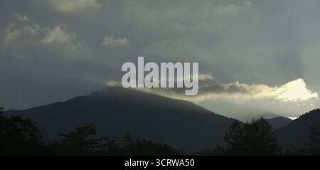 Sun rays pierce through clouds over mountain silhouette at dawn Stock Photo