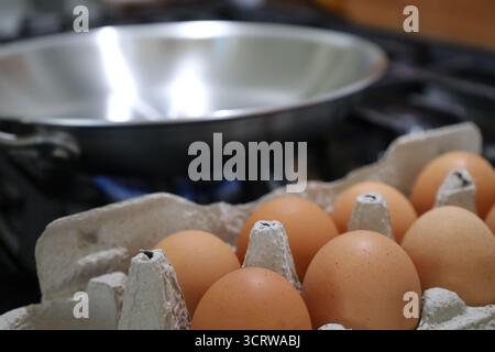 Egg Carton in Foreground with Stainless Steel Skillet on Stove Stock Photo