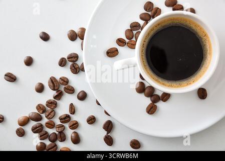 Detail of coffee cup in white ceramic mug on white table with coffee beans. Top view. Stock Photo