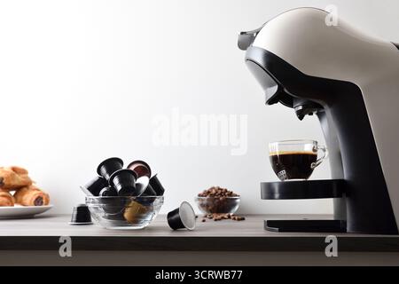 Freshly brewed coffee in an espresso machine on a wooden bench with capsules, beans, and pastries, isolated on a white background. Side view. Stock Photo