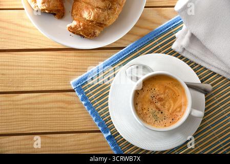 Breakfast with a cup of espresso in a glass and a saucer on a wooden table with bowls of coffee beans, ground coffee, capsules, and pastries. Top view Stock Photo