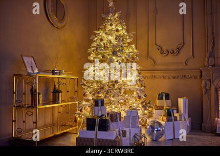 Room decorated to christmas celebration studio. White Christmas tree with white and gold balls in a dark room with a decorative fireplace and candles Stock Photo