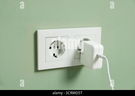 USB adapter with cable plugged into electric socket on green wall, closeup Stock Photo