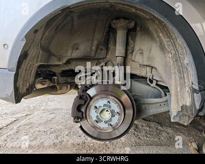 Close-up of disc brake assembly with the wheel removed, showing the caliper, polished rotor, and wheel hub with mounting studs. Stock Photo