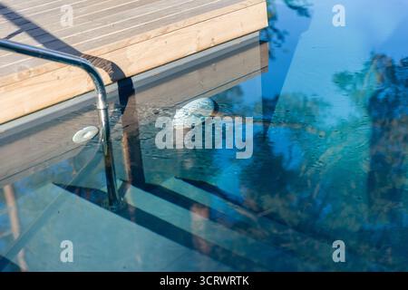 This image captures a sleek swimming pool with a wooden deck, showcasing mesmerizing reflections on the water surface, and creating a tranquil atmosph Stock Photo