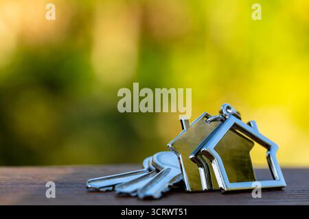 House keys on a house shaped keychain on wooden table, outdoors, close up, copy space. Real estate concept of buying or renting a home Stock Photo
