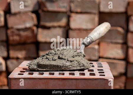 Cement mix or mortar. Cement powder and trowel on red brick at construction site, close up Stock Photo