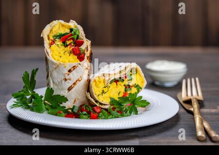 Homemade healthy trendy breakfast eggs burrito with vegetables and herbs in white plate on wooden table, close up. Egg omelette wrapped in a pita brea Stock Photo