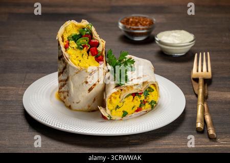 Homemade healthy trendy breakfast eggs burrito with vegetables and herbs in white plate on wooden table, close up. Egg omelette wrapped in a pita brea Stock Photo