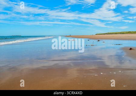 A beautiful view along almost empty Bamburgh Beach wet shoreline wonderful blue sky and cloud reflections Stock Photo