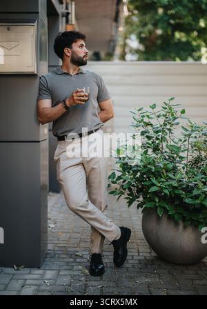 Man relaxing outdoors with a drink in a casual and stylish outfit Stock Photo