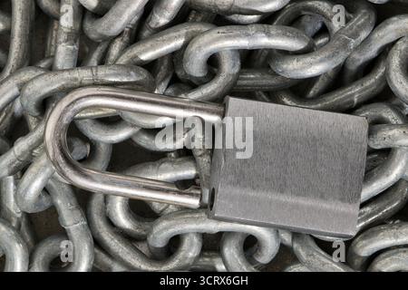 Silver colored padlock unlocked on pile of chains industrial still life security concept. Stock Photo
