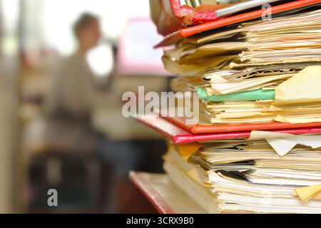 Stack of ring binders, file folders with workplace in the back. Beat the clock, deadlines, urgency, stress concept.Unrecognizable Person,free copy spa Stock Photo