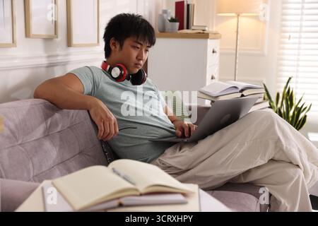 Student with laptop and books preparing for exam on sofa at home Stock Photo
