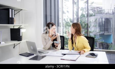 Two happy Asian adult women engaging in a friendly business discussion in a modern office. They collaborate on new ideas and projects with enthusiasm. Stock Photo