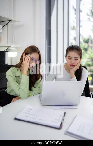 Two adult Asian professionals collaborate on a challenging project experiencing stress in a modern office environment Stock Photo