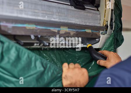 male hand of worker from the cleaning service cleans the air conditioner by spraying water, close-up Stock Photo