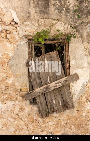 ramshackle old wooden shutter on a Greek building in a poor state of repair hanging from its hinges with the open window behind. Stock Photo