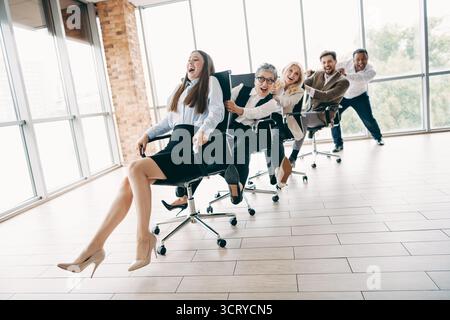 Business team having fun racing on office chairs to foster teamwork and camaraderie in a modern corporate workspace Stock Photo
