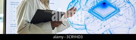 Middle aged Black woman wearing lab coat holding clipboard and pen standing in front of digital brain illustration with microchip discussing artificial intelligence research Stock Photo