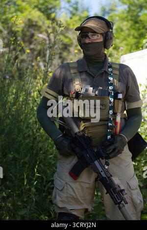 A man in tactical gear prepares his airsoft gun during an outdoor game. Wearing protective goggles, gloves, and a vest Stock Photo