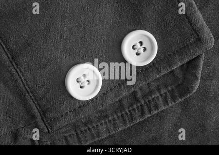 Two white small shirt buttons sewn on black cotton fabric closeup as a background Stock Photo
