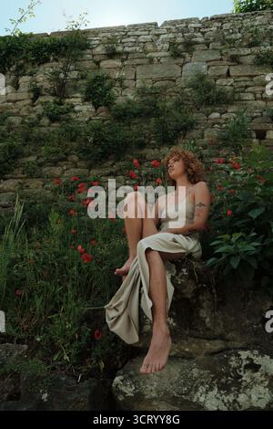 Woman lost in thought sitting by nature wall Stock Photo