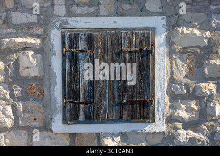 A weathered pair of wooden shutters covers an old stone wall, featuring rusted hinges and chipped paint. The aged texture evokes rural charm, history, Stock Photo