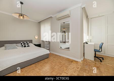 Master bedroom with a king-size bed with a blue velvet upholstered headboard, floating nightstands, and adjustable reading lamps Stock Photo