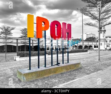 Colorful 'Ipoh' sign sculpture in an urban park with a backdrop of black and white architecture under a dramatic cloudy sky Stock Photo