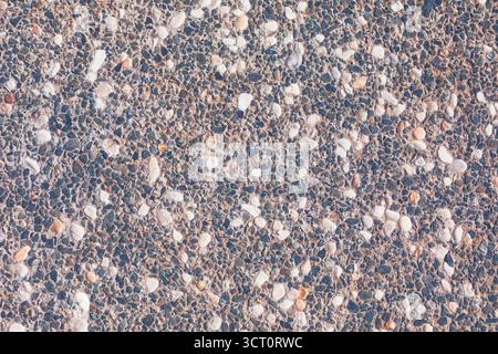 Textured surface exposed aggregate concrete, characterized by numerous small, irregular stones embedded within binder. Varied shades of pebbles create Stock Photo