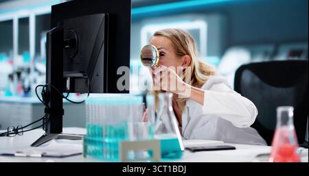 Female Scientist Using Magnifying Glass To Search For Document On Computer In Lab Stock Photo
