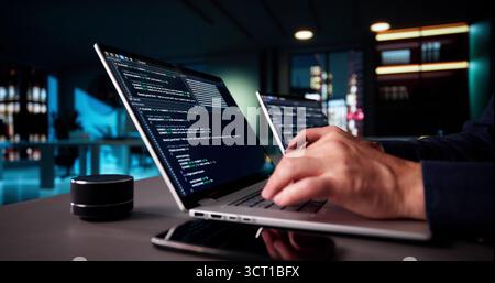 Elderly Senior Programmer Debugging Code On Multiple Laptops At Night. Stock Photo