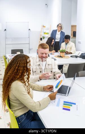 Multicultural business colleagues analyzing financial data and charts on paper and laptop, sharing ideas and discussing project strategies during a co Stock Photo