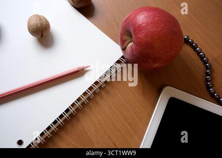 Bright red apple sits next to an empty notebook and pencil on a wooden table. Stock Photo