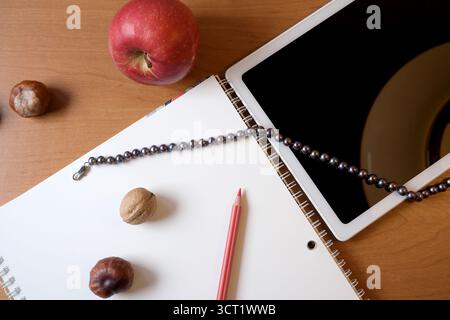 A workspace features an apple, a notebook, and a tablet on a wooden table. Stock Photo