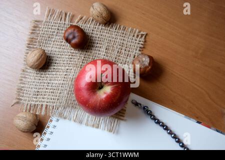 A red apple rests among walnuts on burlap, with a sketchbook nearby and a bracelet. Stock Photo