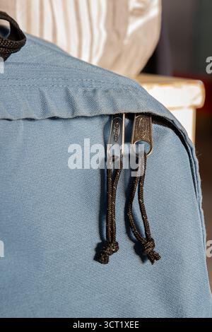 Close-up view of Eastpak backpack showing double zipper pulls with cord attachments on light blue fabric. The metal zipper hardware and cord pulls dem Stock Photo