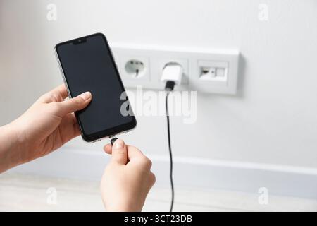 Woman connecting charging cable to smartphone indoors, closeup Stock Photo