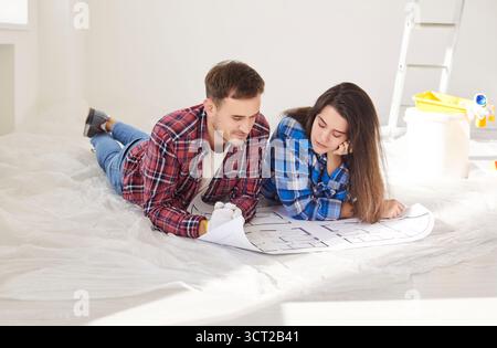 Happy young married couple amuse looking at repair project on paper blueprints, planning work Stock Photo