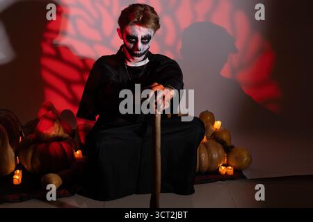 Man is sitting on the floor,holding a staff,with Halloween-themed pumpkins Stock Photo