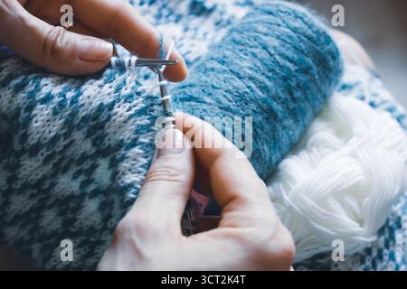 Norwegian knitted pattern in woman hands. Girl holding knitting needles and beautiful knitting pattern. Woman with white and azure knitted pattern. Stock Photo