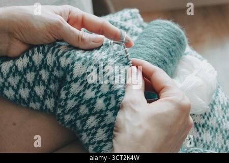 Norwegian knitted pattern in woman hands. Girl holding knitting needles and beautiful knitting pattern. Woman with white and azure knitted pattern. Stock Photo