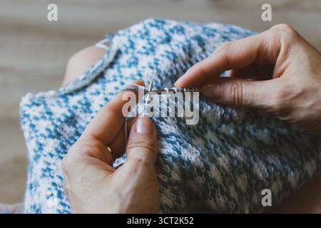 Norwegian knitted pattern in woman hands. Girl holding knitting needles and beautiful knitting pattern. Woman with white and azure knitted pattern. Stock Photo