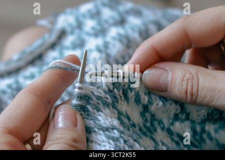 Norwegian knitted pattern in woman hands. Girl holding knitting needles and beautiful knitting pattern. Woman with white and azure knitted pattern. Stock Photo