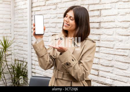 Woman presenting a smartphone with blank screen and smiling. Stock Photo