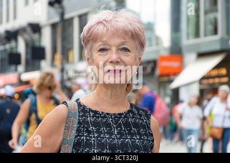 An elegant pensioner aged 65-70 in a stylish dress smiles against the backdrop of a busy city Stock Photo